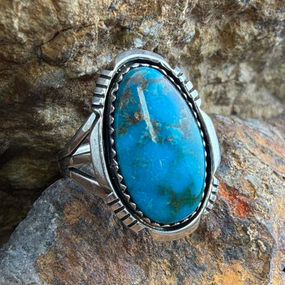 Lone Mountain Turquoise Ring by Ray Coriz - angled front view on rock showing vivid blue oval cabochon with golden matrix and serrated rim