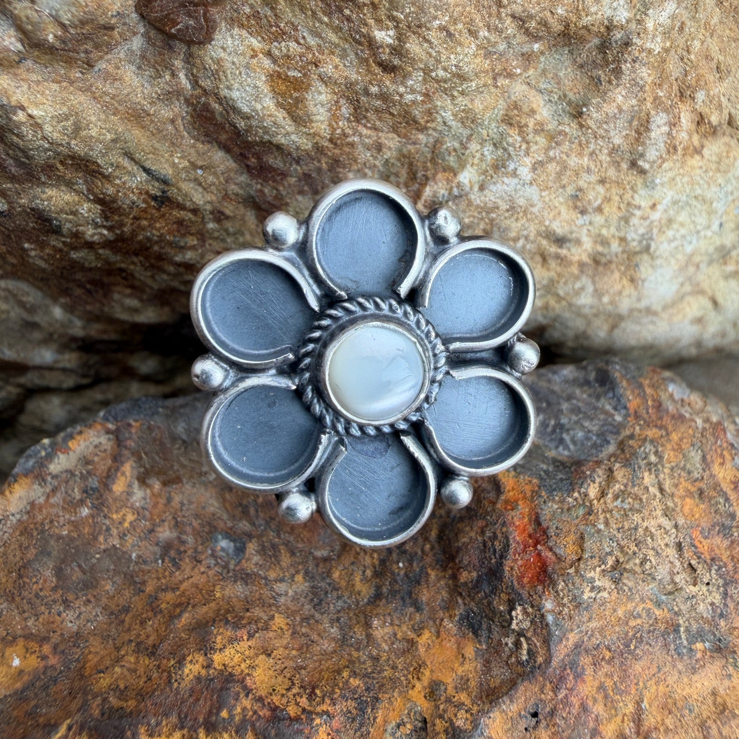 Silver flower-shaped ring on a textured stone surface