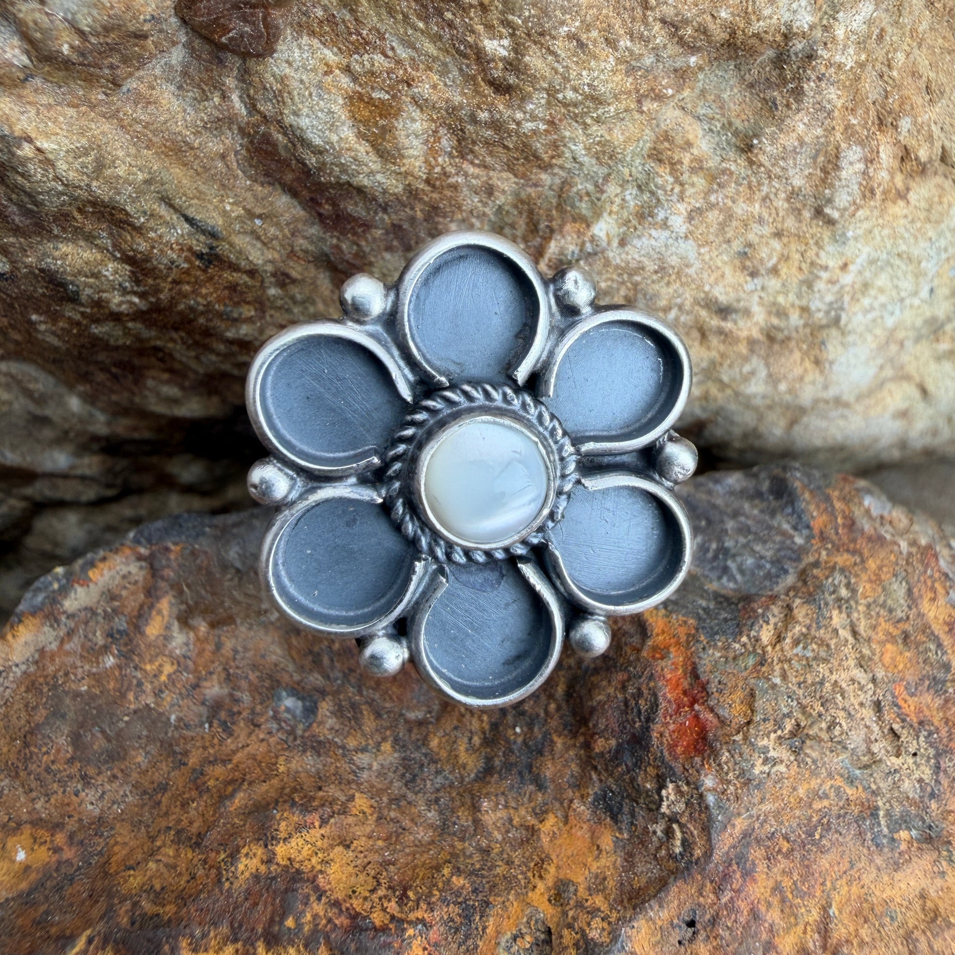 Silver flower-shaped ring on a textured stone surface