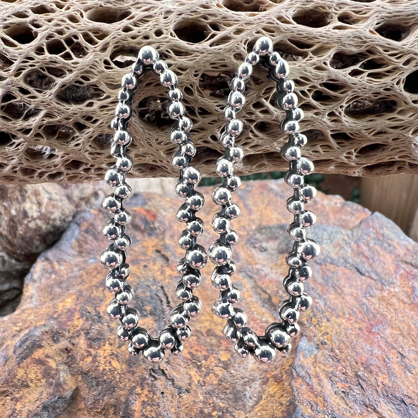 Silver beaded earrings on a textured stone surface