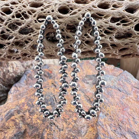 Silver beaded earrings on a textured stone surface