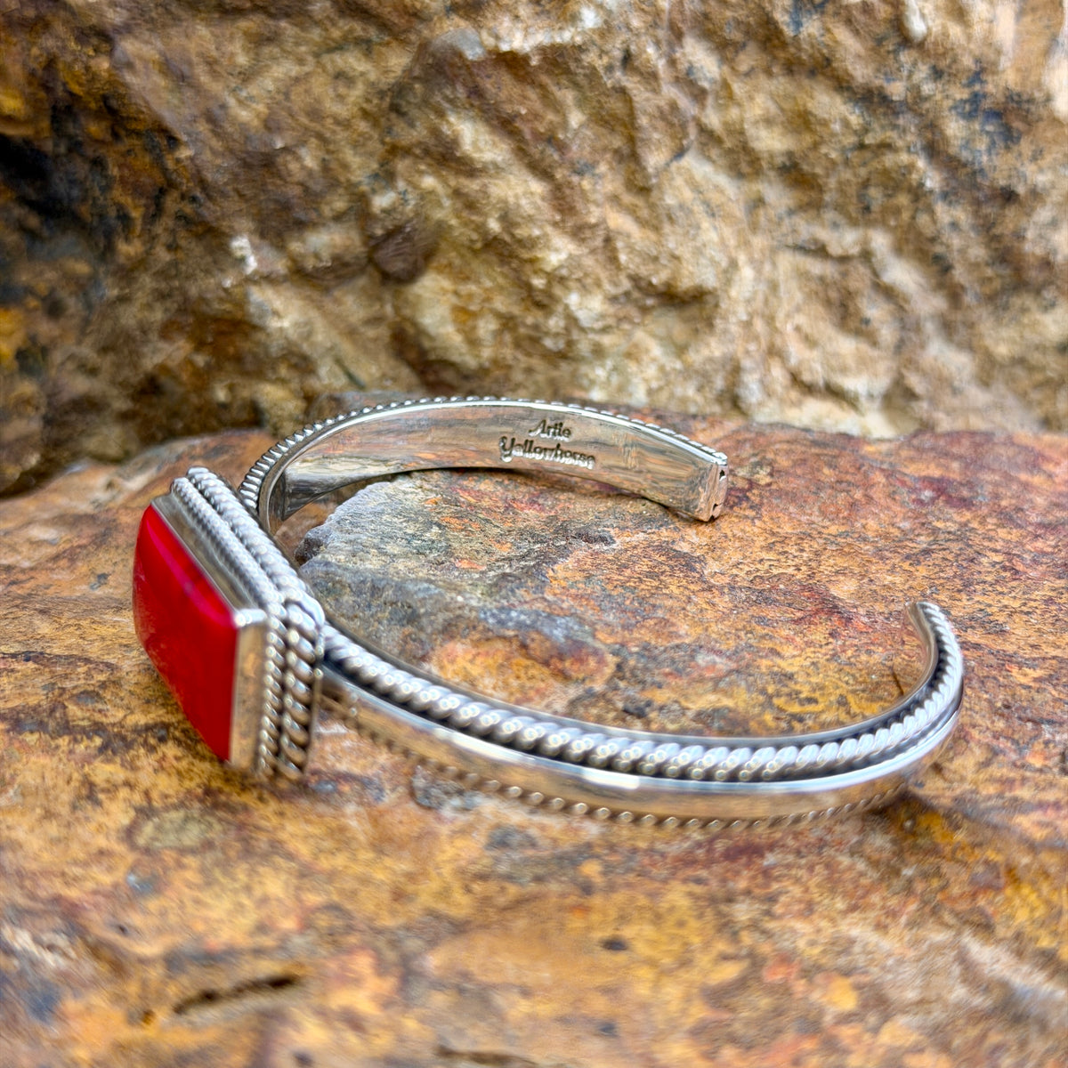Narrow Rosarita Sterling Cuff Bracelet by Artie Yellowhorse, angled view of hallmark on a rock surface.
