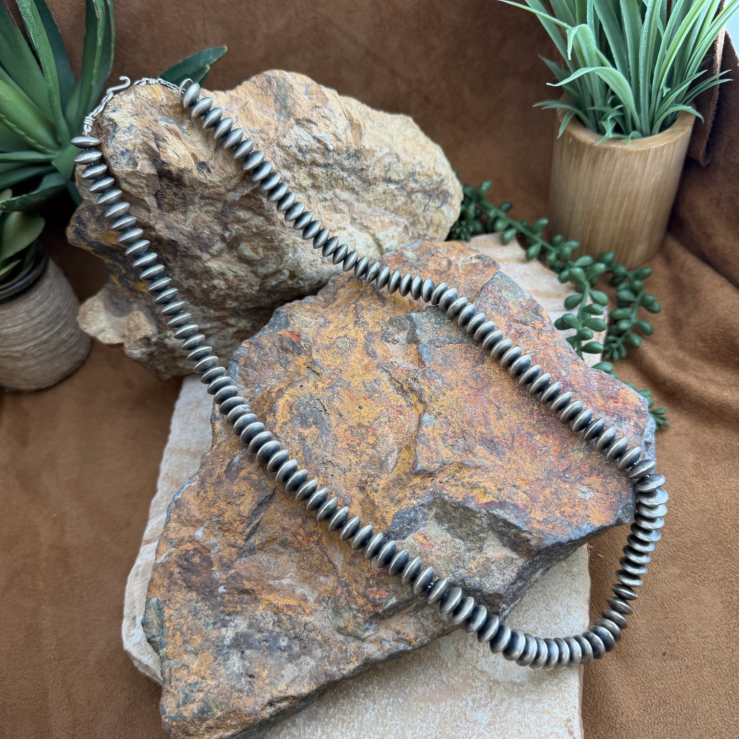 Silver necklace on a rock with plants in the background