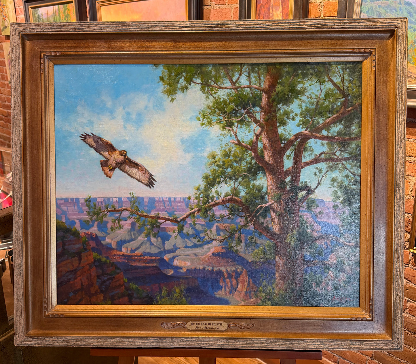 Framed painting of a landscape with a bird flying over a tree and canyon.