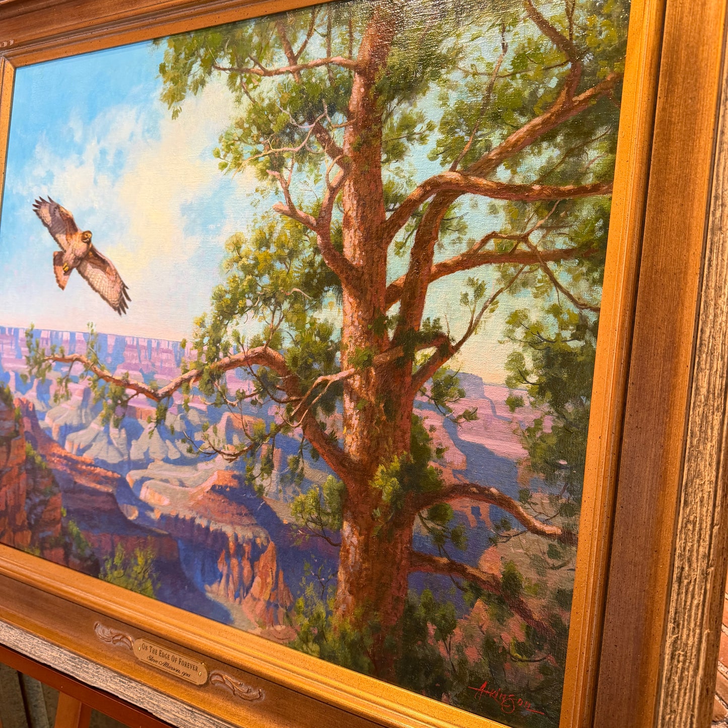 Painting of a tree with a bird flying above a canyon landscape, framed in wood.