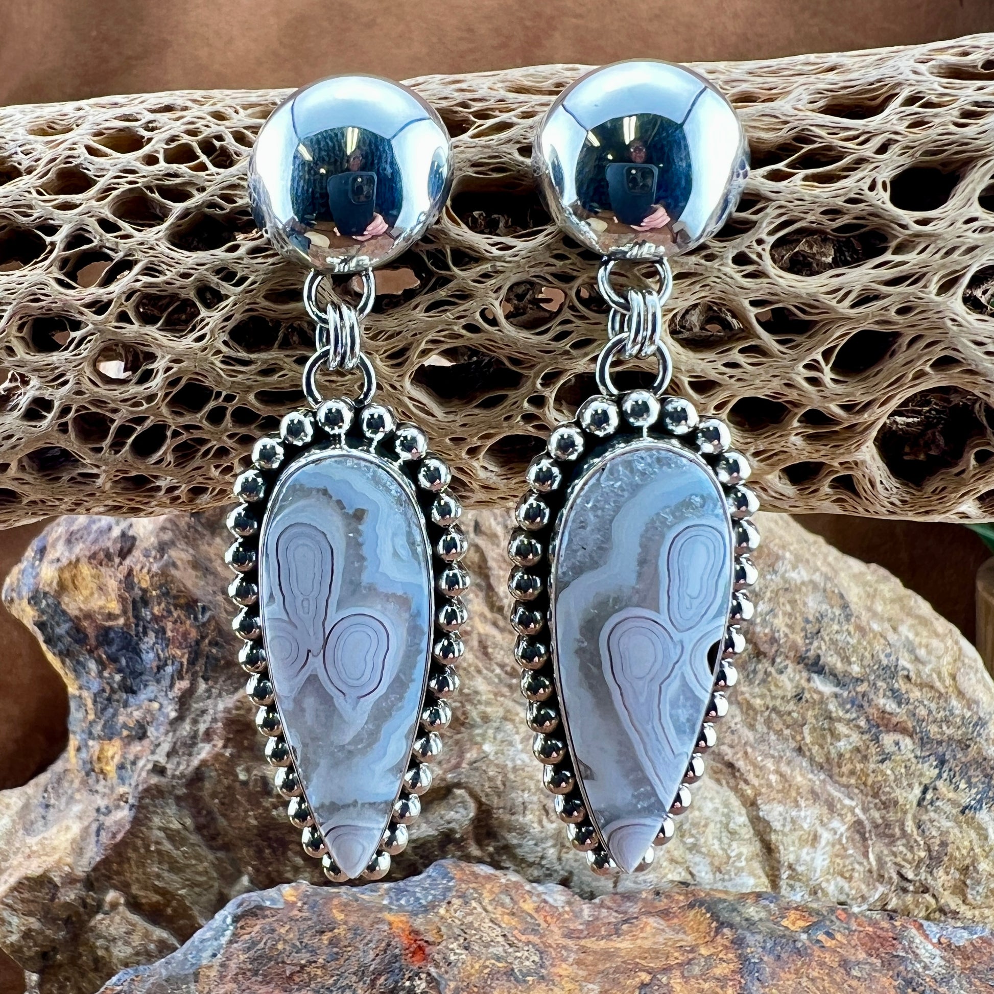 Silver earrings with stone-like designs on a textured surface