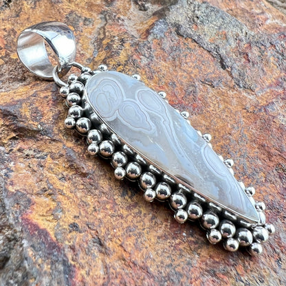 Silver pendant with engraved design on a textured stone background