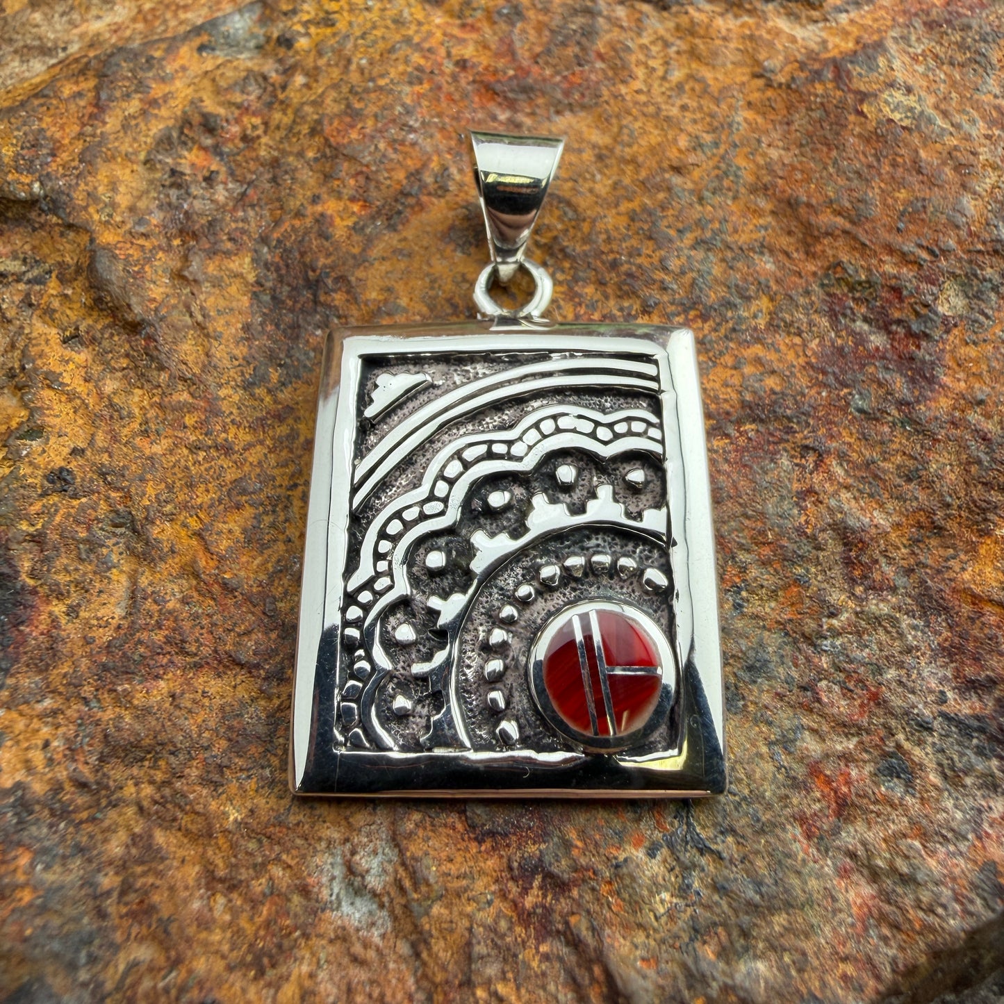 Silver pendant with red stone on a textured brown surface