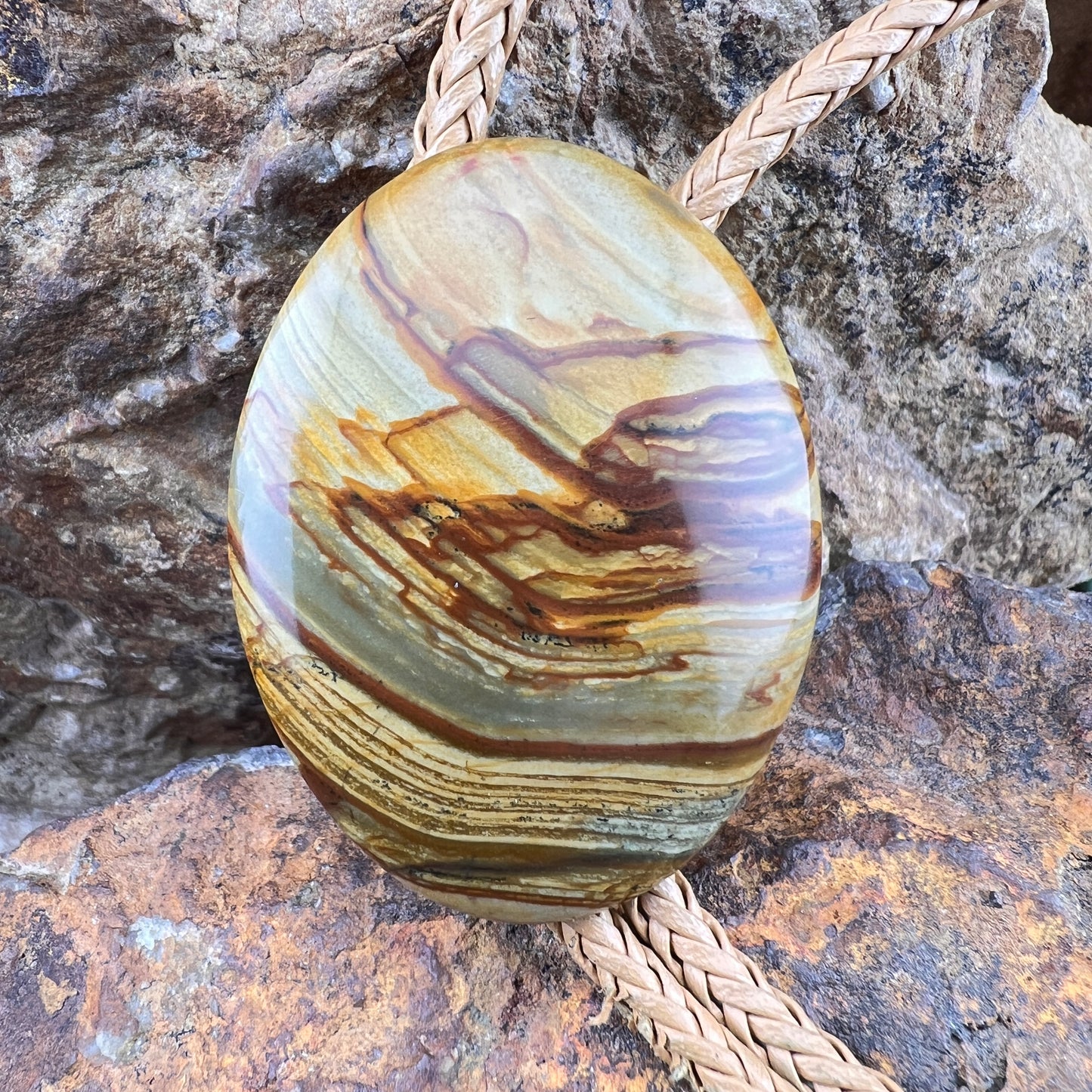 Polished stone pendant with a rope on a rocky background