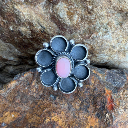 Silver flower shaped ring with a pink stone on a rocky surface