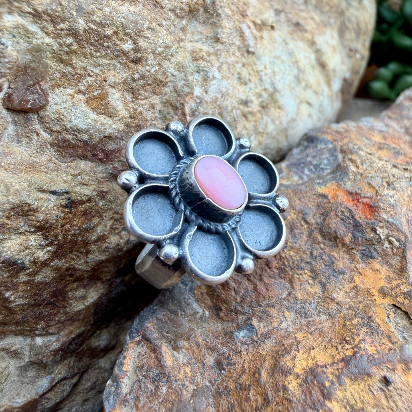 Silver floral shaped ring with a pink stone on a rock background