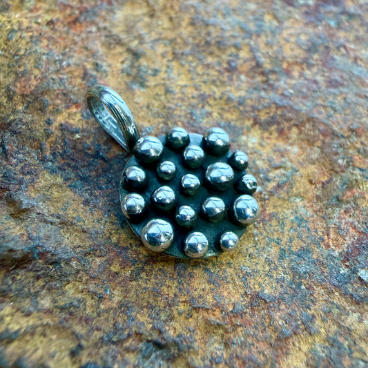 A sterling silver pendant with a cluster of polished dome beads on a dark backing, resting on a textured brown and gold rock surface.