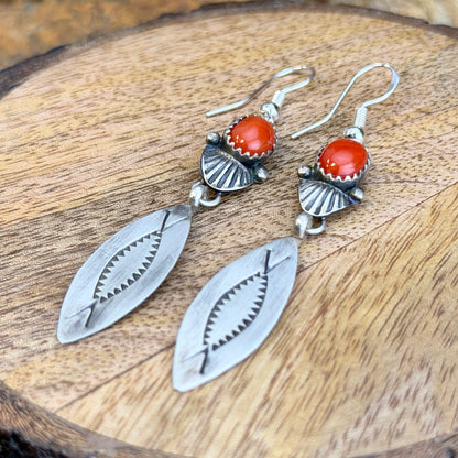 Mary Tso red coral dangle earrings displayed on wood
