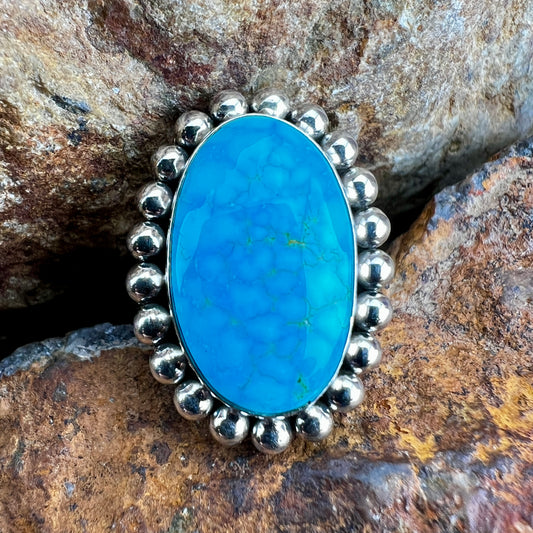Turquoise stone ring with silver beaded setting on a stone background
