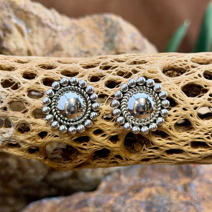sterling silver dome earrings surrounded by inner twisted rope border and outer silver beads by artie yellowhorse. they hang on a piece of driftwood.