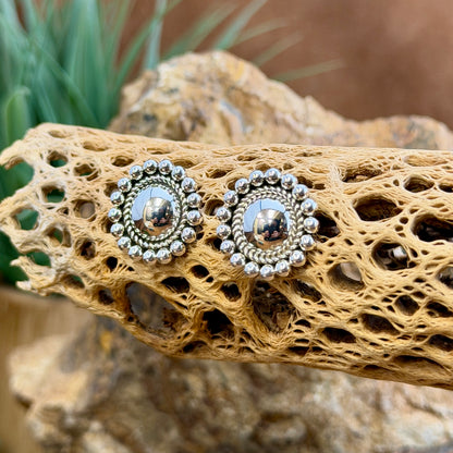 sterling silver dome earrings surrounded by inner twisted rope border and outer silver beads by artie yellowhorse. they hang on a piece of driftwood.