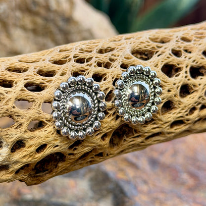 sterling silver dome earrings surrounded by inner twisted rope border and outer silver beads by artie yellowhorse. they hang on a piece of driftwood.