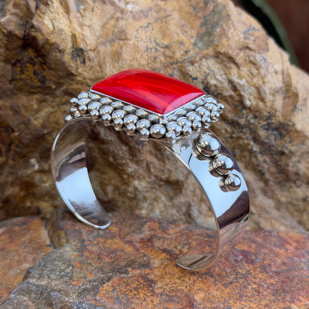 Rosarita Statement Cuff Bracelet by Artie Yellowhorse, front side view on a rocky surface. 