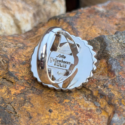 Sterling Silver ring by Artie Yellowhorse. large oval dark blue cabochon surrounded by rope border and silver beads. it rests on a rocky surface. this one showcases the back of the ring with stamped artist and "sterling"
