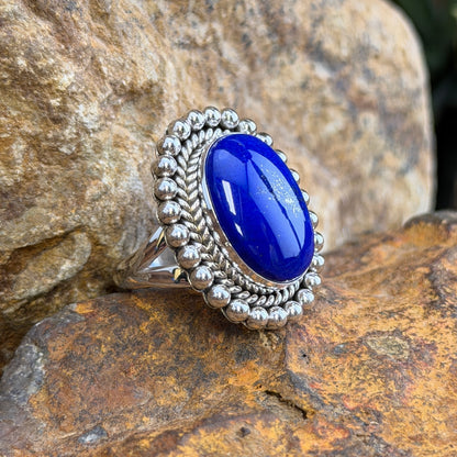 Sterling Silver ring by Artie Yellowhorse. large oval dark blue cabochon surrounded by rope border and silver beads. it rests on a rocky surface