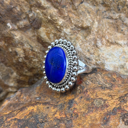 Sterling Silver ring by Artie Yellowhorse. large oval dark blue cabochon surrounded by rope border and silver beads. it rests on a rocky surface