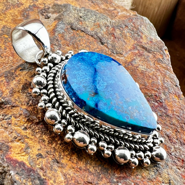 Silver pendant with a blue stone on a textured stone surface