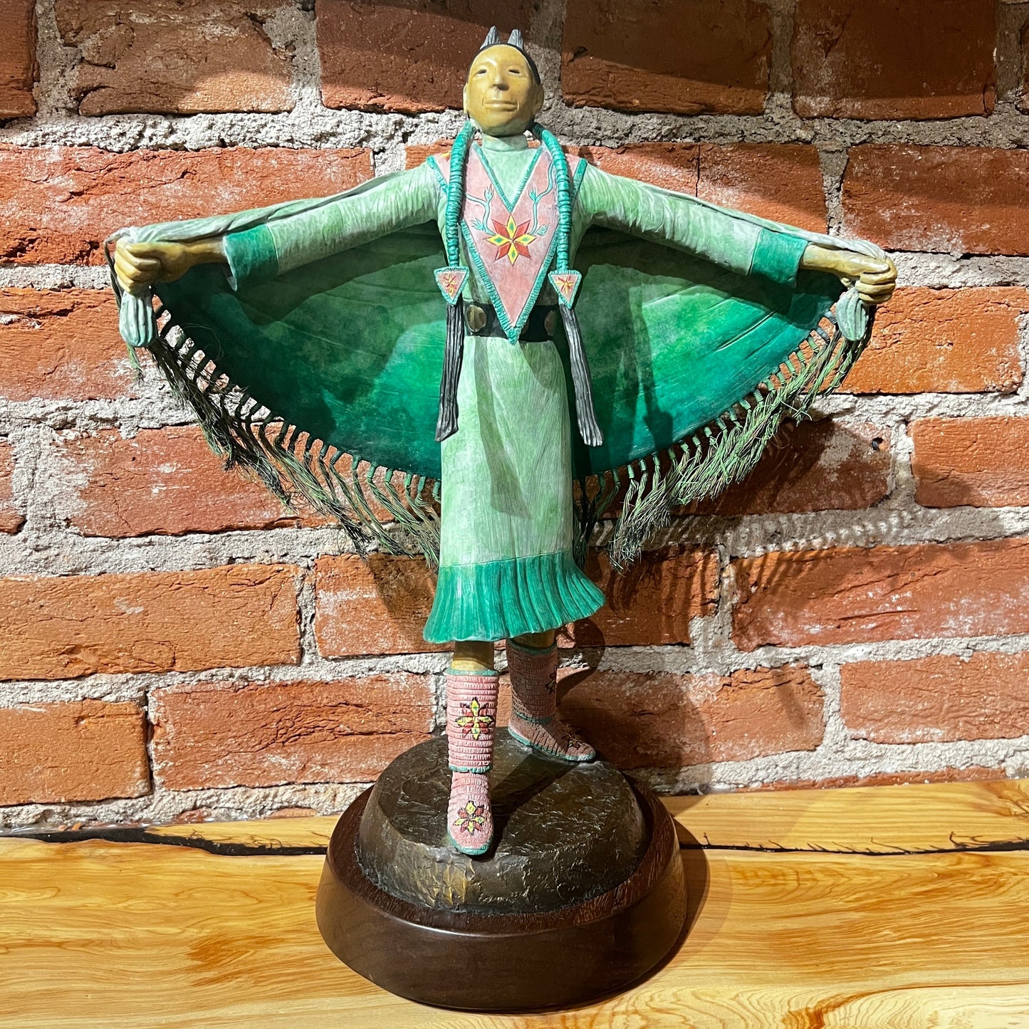 Statue of a figure in traditional attire against a brick wall.