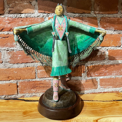 Statue of a figure in traditional attire against a brick wall.