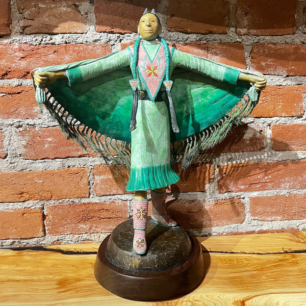 Statue of a figure in traditional attire against a brick wall.