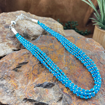 Blue beaded necklace on a textured stone surface with plants in the background