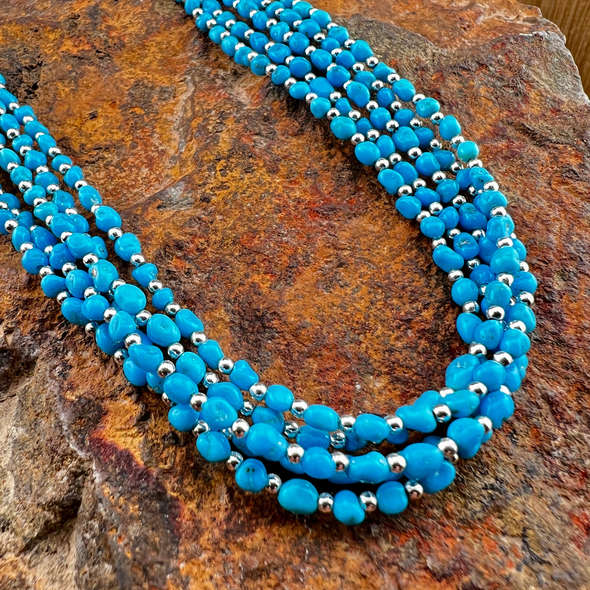 Blue beaded necklace with silver accents on a textured stone surface
