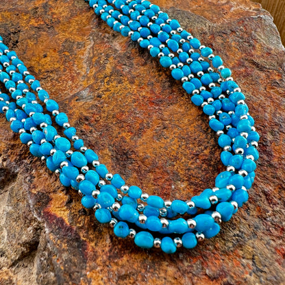 Blue beaded necklace with silver accents on a textured stone surface