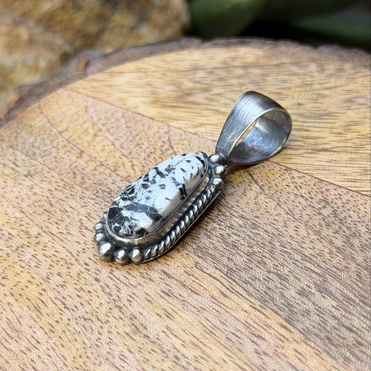 A sterling silver pendant featuring a black-and-white marbled stone cabochon, resting on a textured wooden surface.