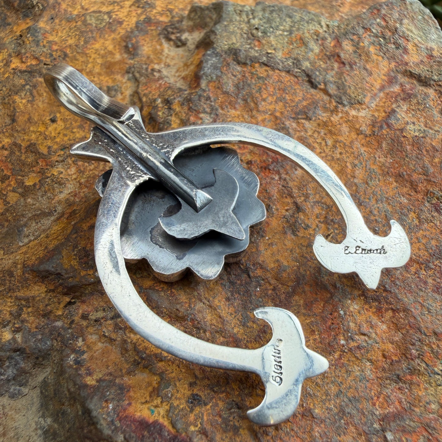 Back of a silver naja shaped pendant with stamping on it. "Sterling" "E. Enoah"
