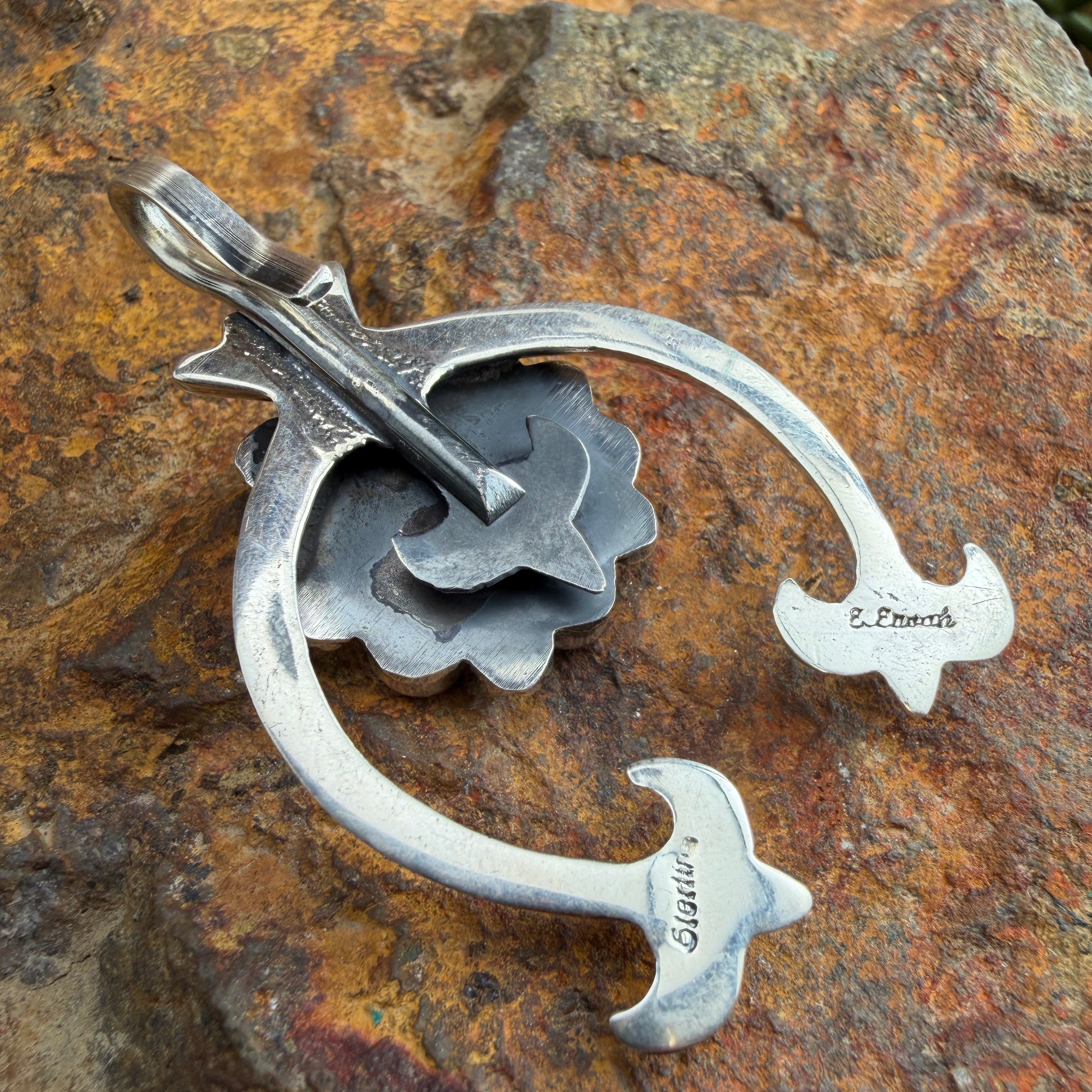 Back of a silver naja shaped pendant with stamping on it. "Sterling" "E. Enoah"
