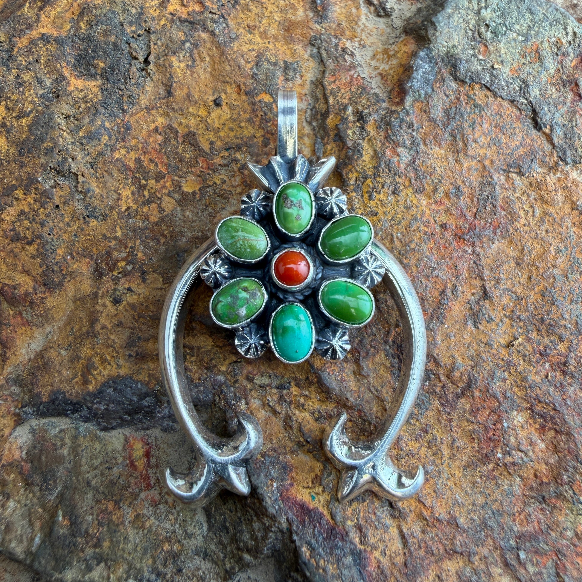 Silver pendant with green and red stones on a stone background