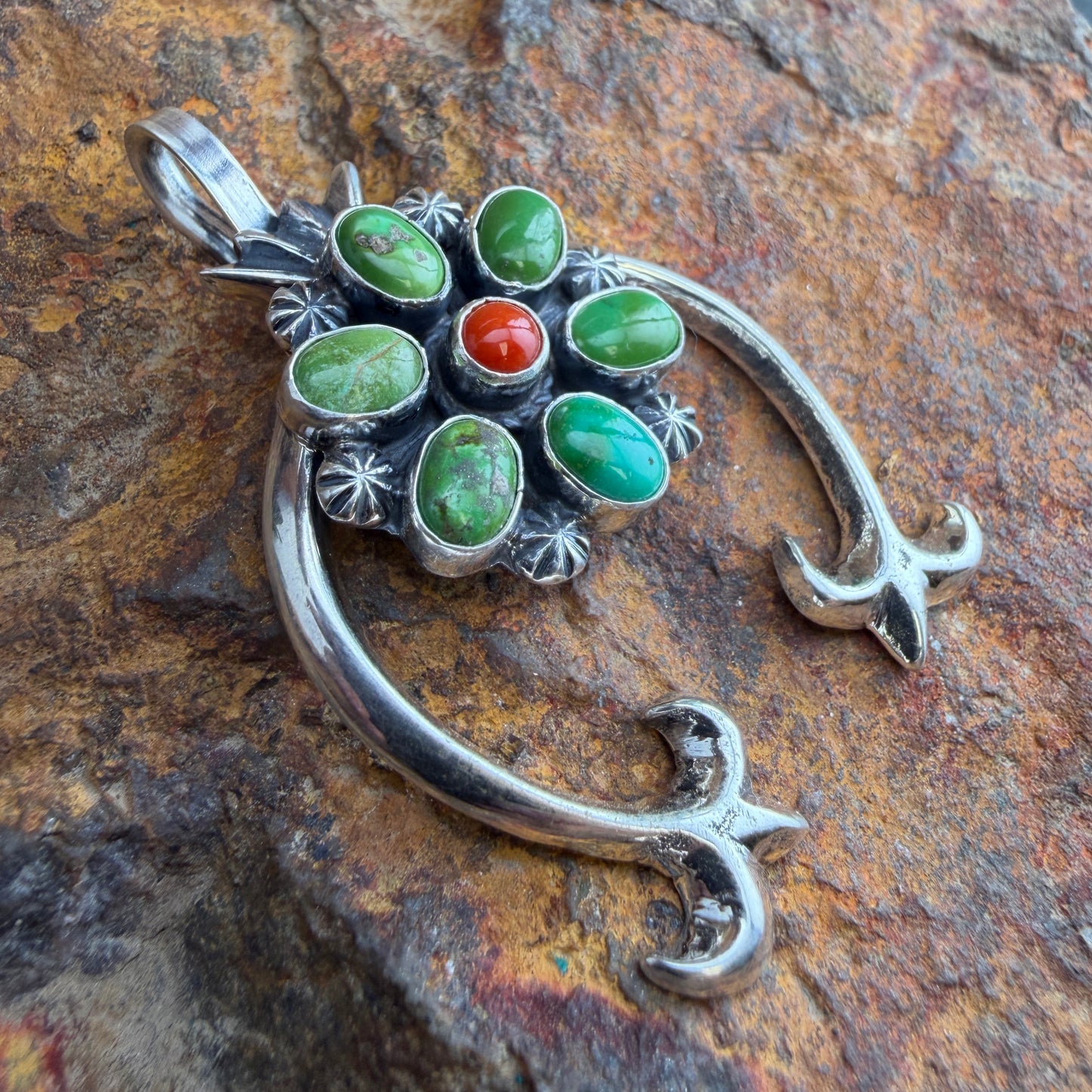 Silver pendant with green and red stones on a stone surface