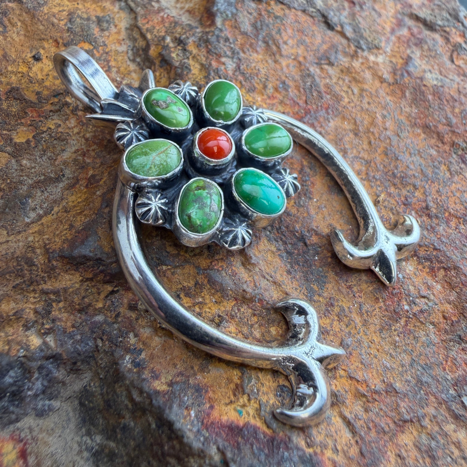 Silver pendant with green and red stones on a stone surface