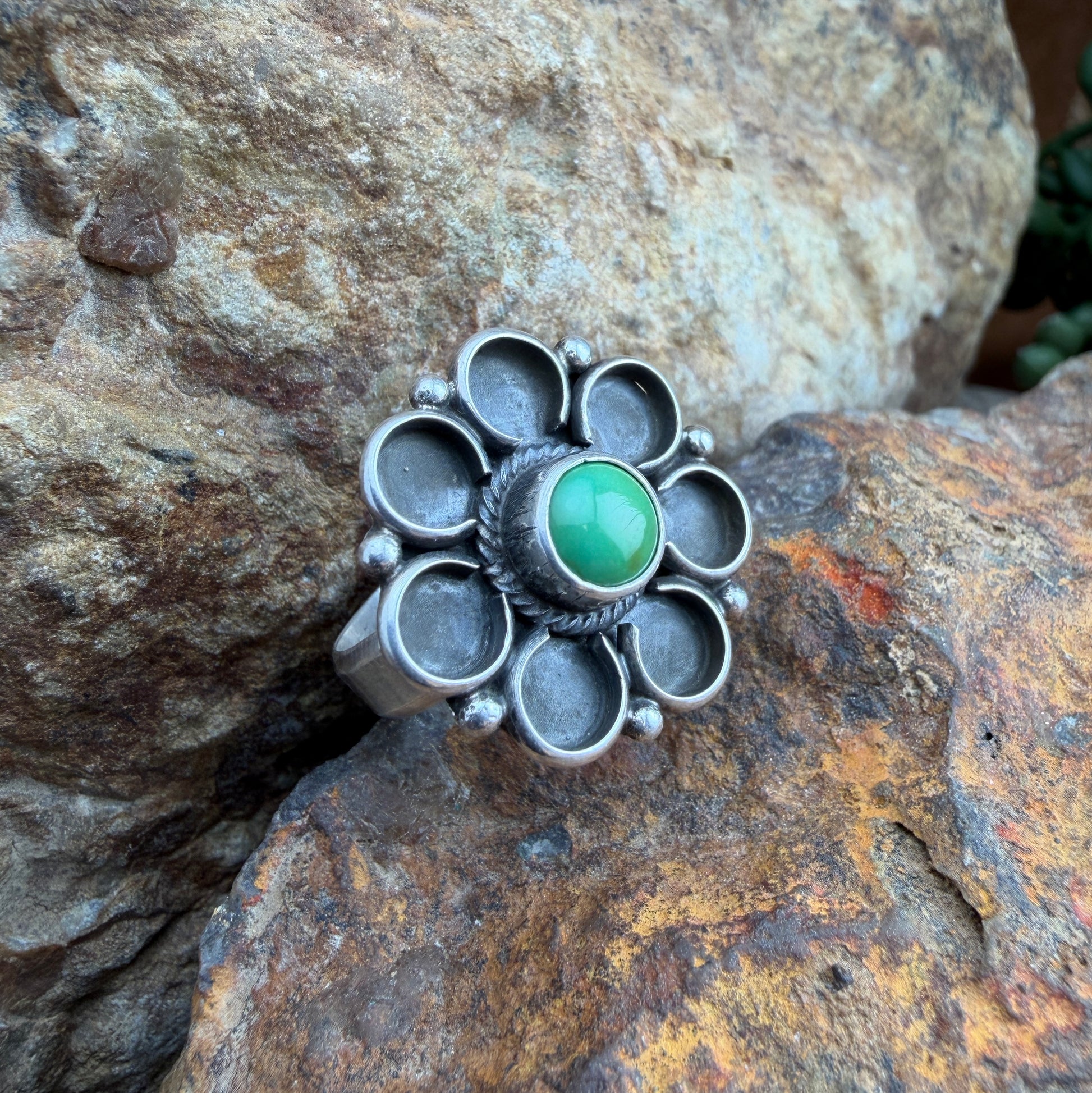 Silver flower ring with a green stone on a rocky surface