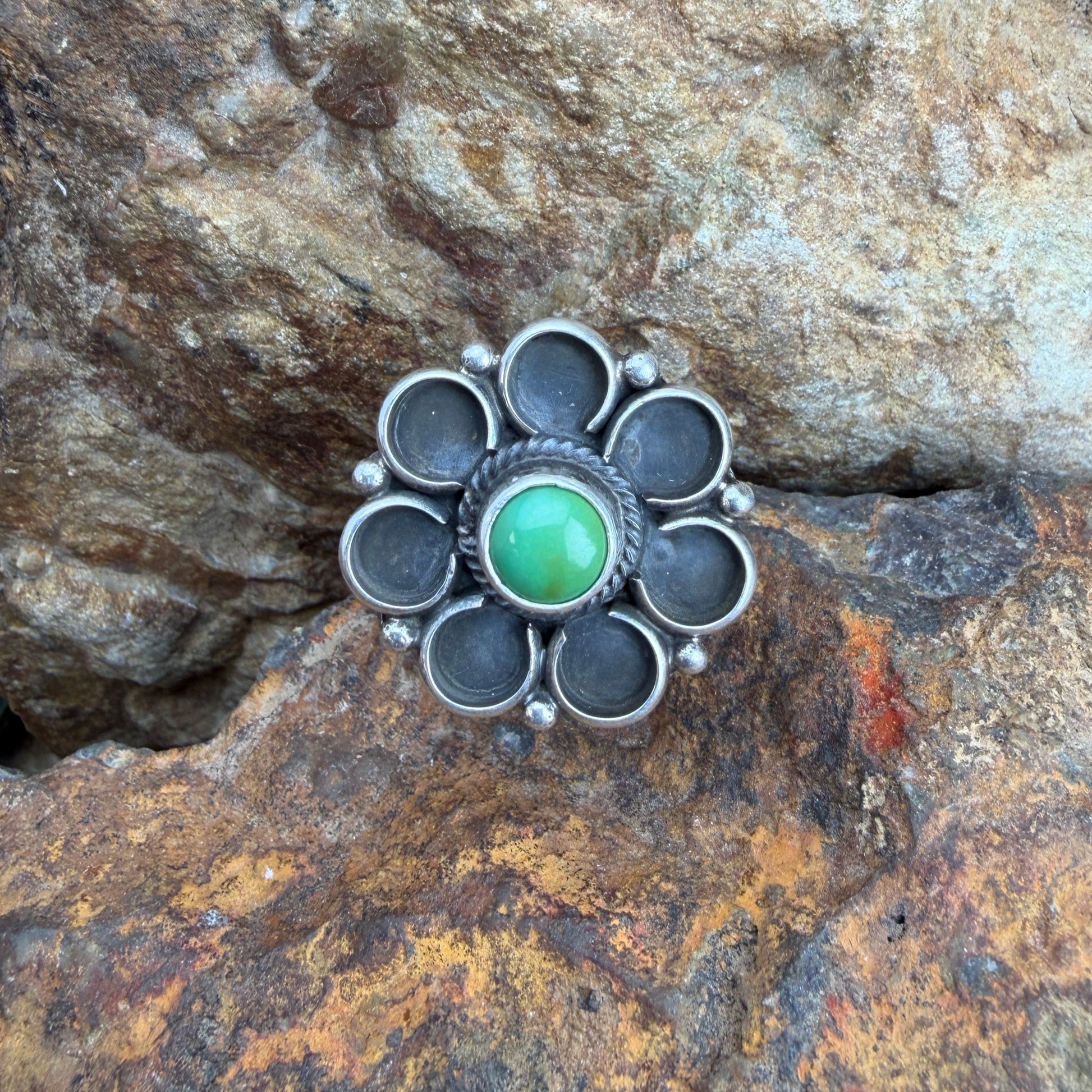 Silver flower ring with a green gemstone on a rocky surface