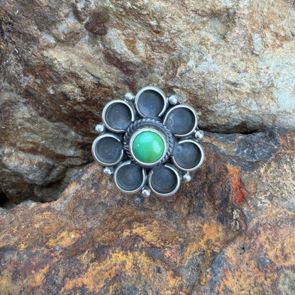 Silver flower ring with a green gemstone on a rocky surface