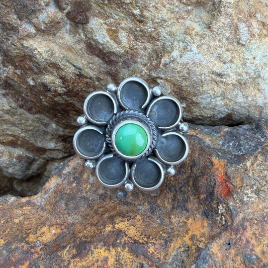 Silver flower ring with a green gemstone on a rocky surface