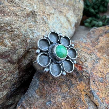 Silver flower ring with a green stone on a rocky surface