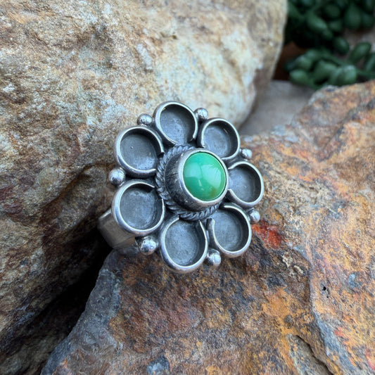 Silver flower ring with a green stone on a rocky surface