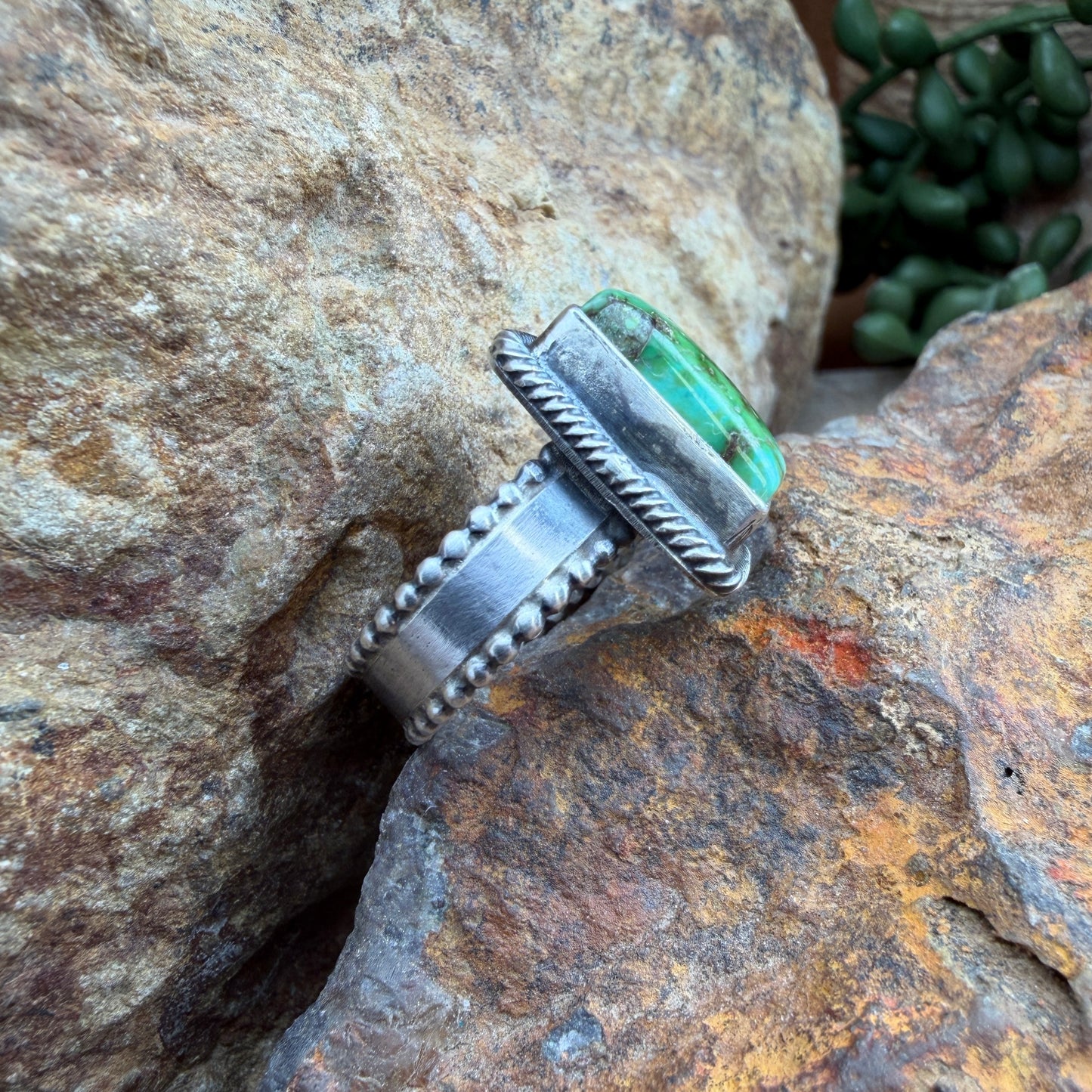Silver ring with a green stone on a rocky surface