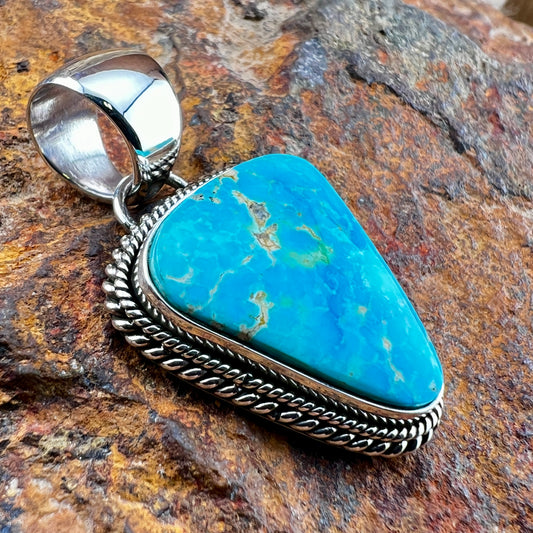 Turquoise pendant with silver setting on a stone background