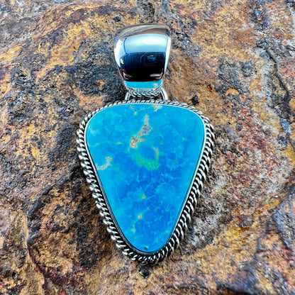 Turquoise stone pendant with silver setting on a textured stone background