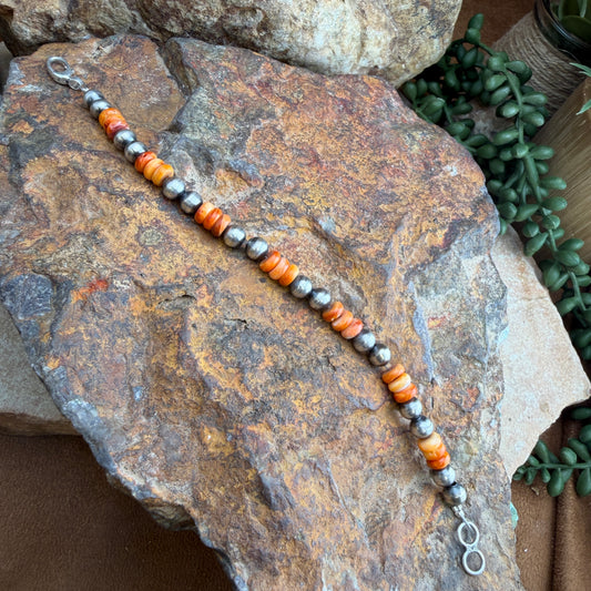 Beaded bracelet with orange and gray beads on a rock background