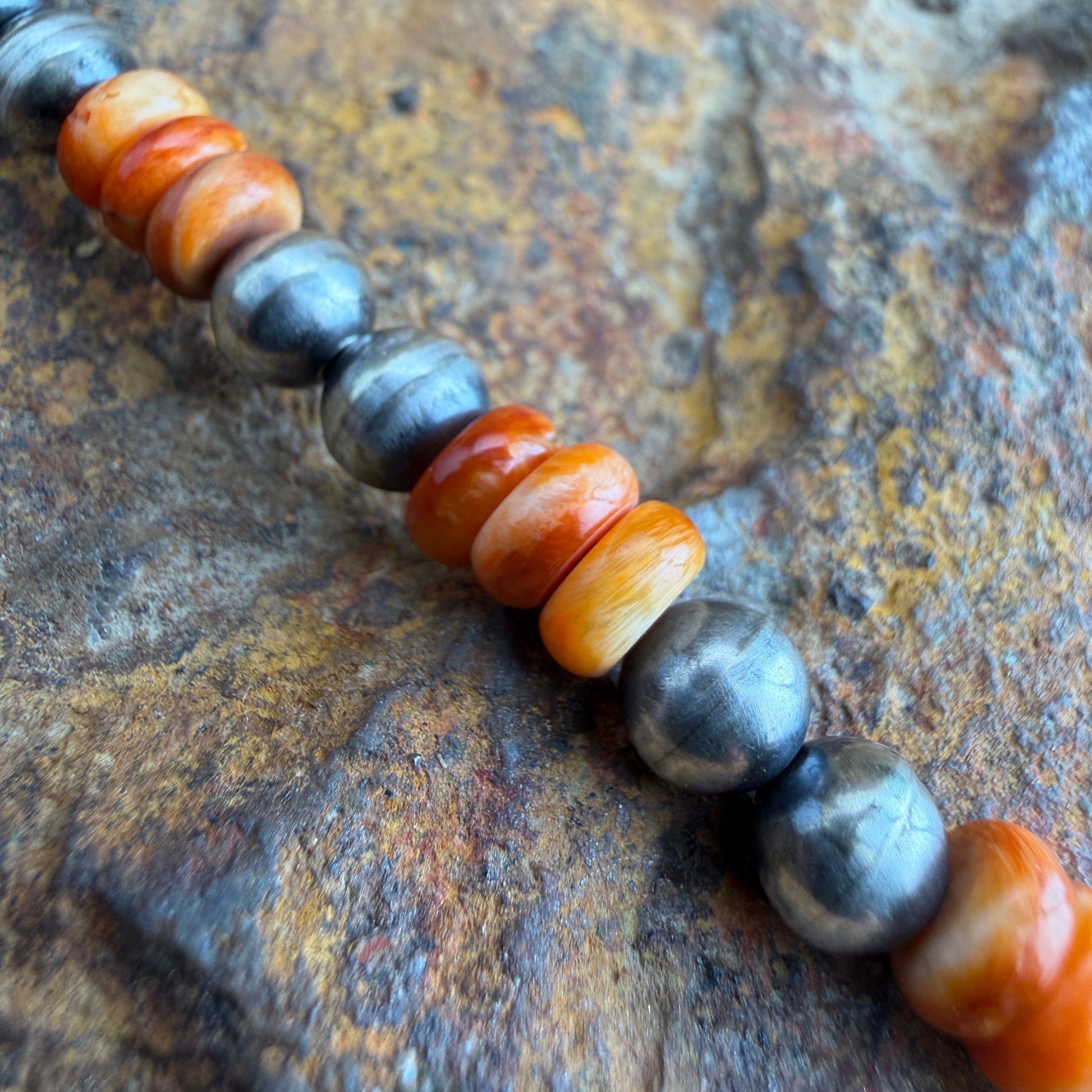 Beaded bracelet with orange and gray beads on a textured surface