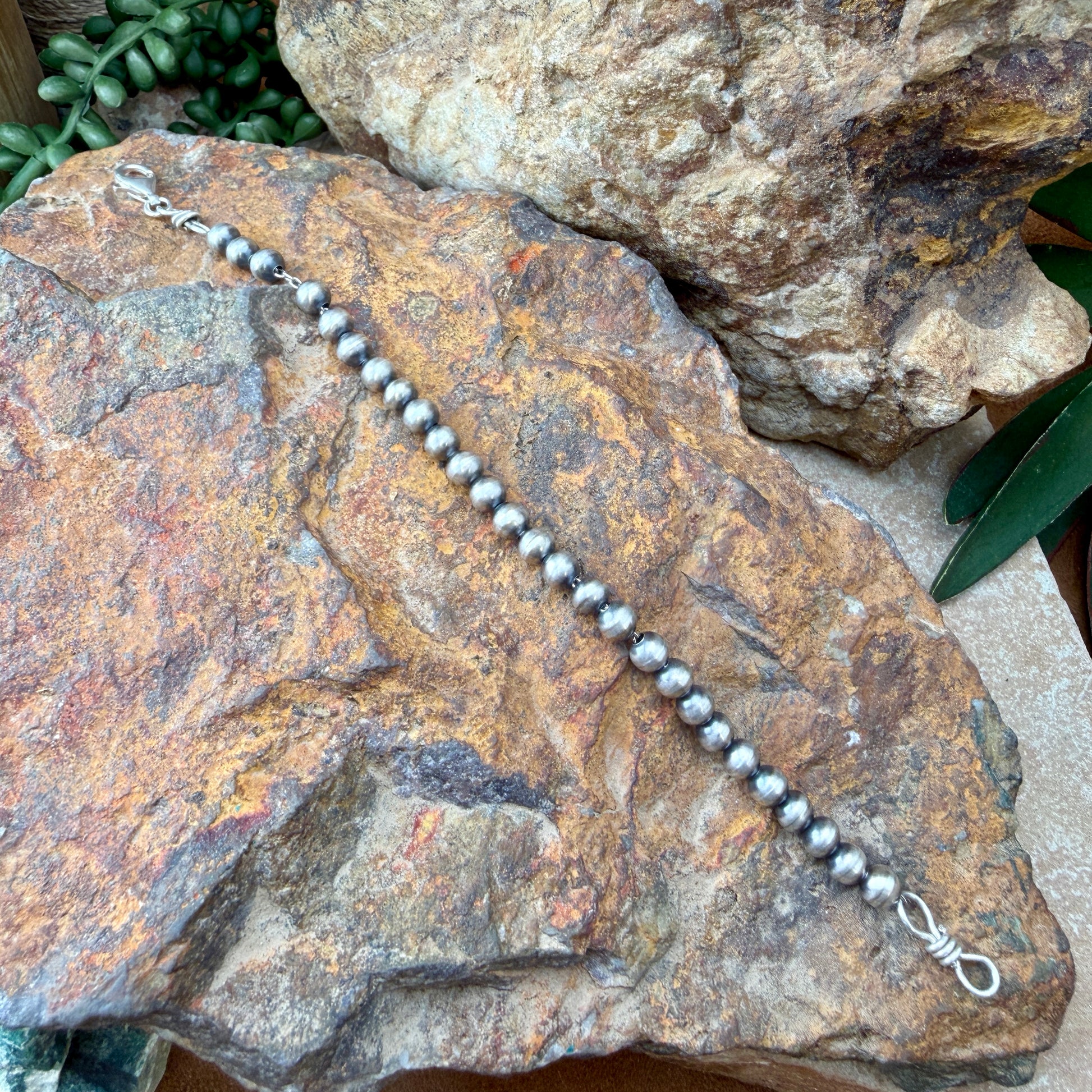Silver beaded bracelet on a textured stone surface with greenery in the background